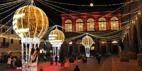 Luci scintillanti e palloni luminosi creano un'atmosfera magica per un week end a Rimini. Persone passeggiano su un tappeto rosso, ammirando le decorazioni natalizie.