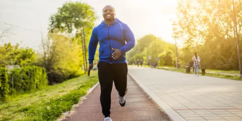 Glücklicher Mann beim Laufen im Park. Sein Training laufen im Sonnenschein macht ihn fit und gesund.