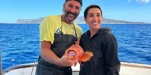 Coppia felice in barca, lui mostra un pesce rosso appena pescato, un'esperienza di pesca turismo indimenticabile.