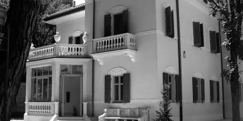 Villa Franceschi a Riccione, un'elegante dimora con balconi e un ingresso accogliente, circondata da alberi e un giardino curato.