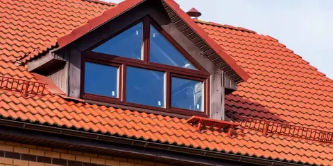 Ein Dachfenster mit dreieckigem Oberlicht und roten Ziegeln. Informieren Sie sich, was kostet eine gaube für Ihr Haus.