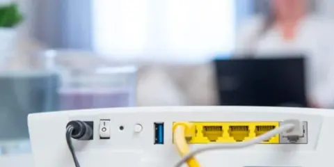 Router vom Strom trennen wie lange? Das Bild zeigt die Rückseite eines weißen Routers mit Netzteilanschluss, Schalter und LAN-Ports.