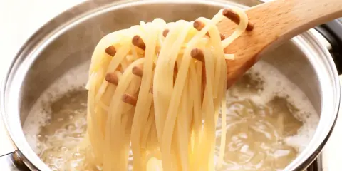 Une louche en bois retire des spaghettis bouillis à la perfection, juste al dente, d'une casserole d'eau bouillante.