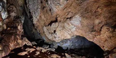 Wnętrze jaskini mylnej, z kamienistym dnem i skalnymi ścianami o rdzawym zabarwieniu, tworzącymi naturalne sklepienie.