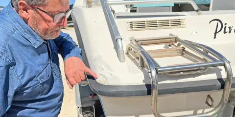Un homme examine les dégâts sur le gelcoat d'un bateau. C'est quoi le gelcoat ? C'est la couche protectrice extérieure.
