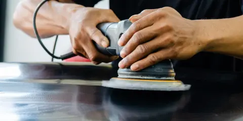 Mains polissant une surface sombre avec une ponceuse orbitale pour polir aluminium rayé.