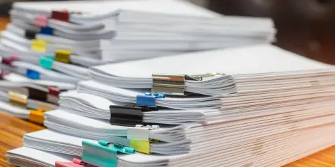 Piles de documents, certains reliés par des pinces colorées, prêts pour le service de la publicité foncière.