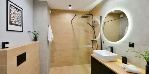 Baño moderno con ducha de suelo continuo, lavabo sobre encimera y espejo circular iluminado.