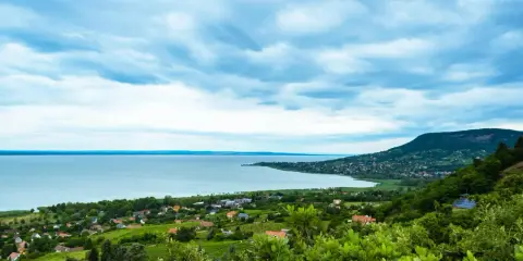 Widok na Balaton z góry, z zielonymi wzgórzami i domkami. W oddali widać jezioro i plażę.