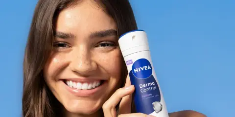 Donna sorridente con prodotto Nivea Derma Control, ideale per chi soffre di bruciore sotto le ascelle.