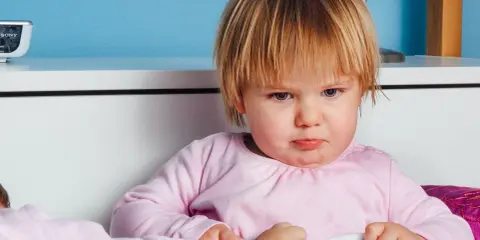 Smutna dziewczynka w różowej bluzce, być może z powodu nietolerancji laktozy, siedzi w łóżku.