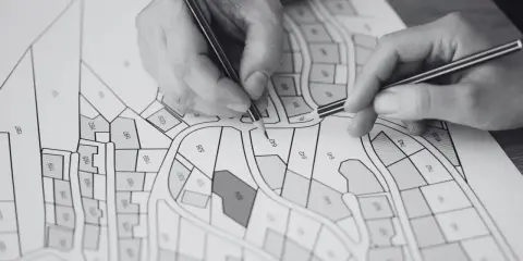 Ręce analizują mapę działek z numerami. Sprawdzenie, jak sprawdzić czy mieszkanie jest zadłużone, wymaga analizy dokumentów.
