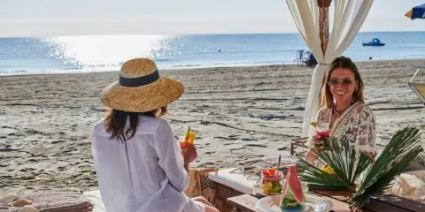 Due donne sorseggiano cocktail in un bagno Jacarè a Cervia, godendosi la spiaggia e il mare.