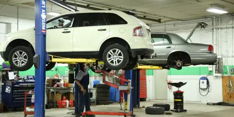 Mecánico trabajando en un taller con vehículos elevados, usando herramientas para neumáticos y otros equipos.
