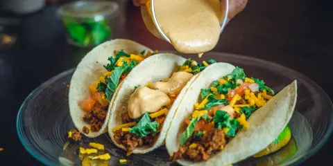 Tre läckra tacos med köttfärs, grönsaker och ost. En krämig sås hälls över dem, perfekt mexikansk mat.