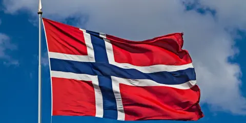 Norweska flaga powiewa na wietrze. W tle błękitne niebo z chmurami. Takie są prace, gdy jest piękna pogoda.