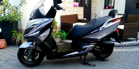 Elegancki skuter Kymco Dink 50 w kolorze grafitowym stoi na podjeździe, gotowy do jazdy.