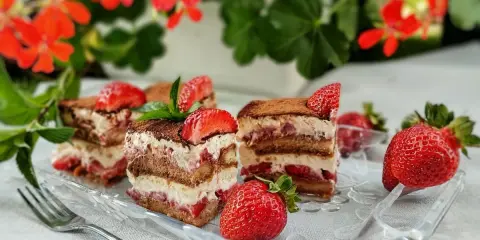 Pyszne tiramisu truskawkowe z warstwami biszkoptu, kremu i świeżych truskawek, posypane kakao i udekorowane owocami.