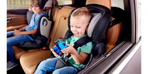 Uśmiechnięty chłopiec bawi się zabawką w foteliku Kinderkraft Comfort Up ADAC. Obok siedzi starszy brat.