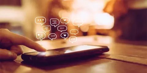 Palec dotyka ekranu telefonu, a nad nim pojawiają się dymki czatu. Dowiedz się, jak odzyskać wiadomości z kosza w telefonie.