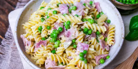 Fusilli-Nudeln mit Erbsen und Schinken in einer cremigen schinken sahne sauce, bestreut mit schwarzem Pfeffer.