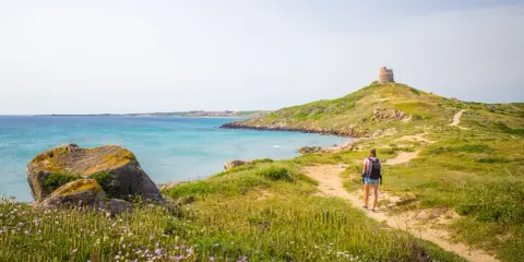 Sentiero panoramico per un tour Sardegna 7 giorni, con torre antica e mare turchese.