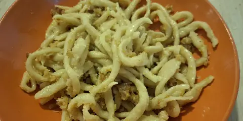 Pici fatti in casa con un saporito sugo per i pici, serviti in un piatto arancione.