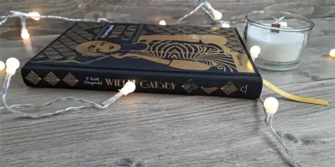 Książka "Wielki Gatsby" F. Scotta Fitzgeralda, otoczona świątecznymi lampkami, zaprasza do odkrycia jej streszczenia i historii.