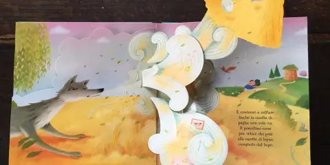 Libri pop-up più belli: un lupo soffia su una casetta di paglia, mentre un maialino corre verso una casetta di legno.