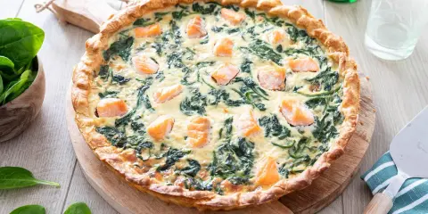 Une délicieuse quiche saumon épinard, dorée et garnie de morceaux de poisson et de légumes verts, prête à être dégustée.