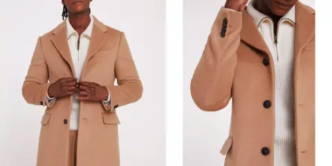 A man models a stylish camel coat, perfect for wearing with a suit. The coat features dark buttons and a classic lapel.