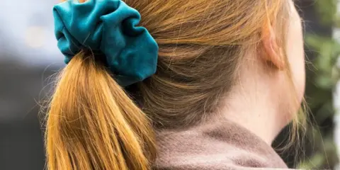 En hästsvans med en turkos scrunchie i sammet. Håret är kopparfärgat och faller mjukt.