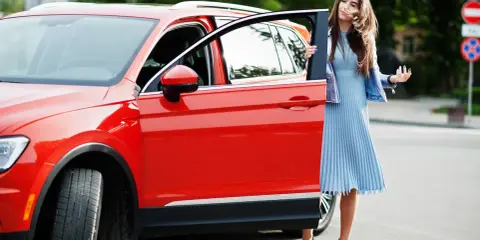 Mujer elegante sale de un monovolumen o SUV rojo brillante.