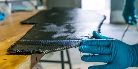 Main d'une personne en gant bleu manipulant un tissu de carbone imbibé de résine, une étape clé pour comprendre qu'est-ce que l'epoxy dans la fabrication composite.