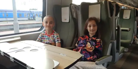 Dzieci siedzą w przedziale dla osoby z dzieckiem do lat 6 Intercity. Chłopiec w kolorowym T-shircie i dziewczynka w kurtce z kwiatowym wzorem.