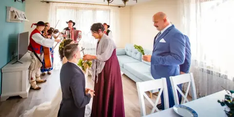 Wzruszający moment błogosławieństwa rodziców. Panna młoda klęczy, a matka z córką udzielają jej błogosławieństwa. W tle gra kapela góralska.