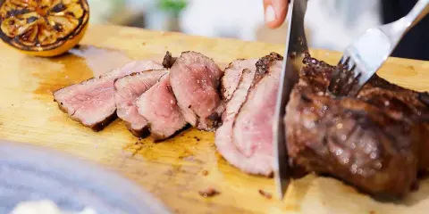 Perfekt grillad ryggbiff skärs upp på en skärbräda. Bredvid ligger en grillad citronhalva.