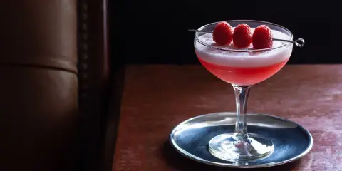 Ein eleganter Clover Club Cocktail mit Himbeeren auf einem silbernen Untersetzer, bereit zum Genuss.