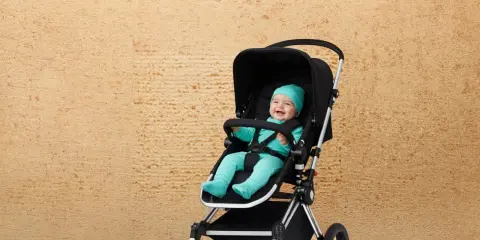 Uśmiechnięte dziecko w turkusowym ubranku siedzi w czarnej spacerówce. Idealne spacerówki dla dzieci na pierwsze wycieczki.