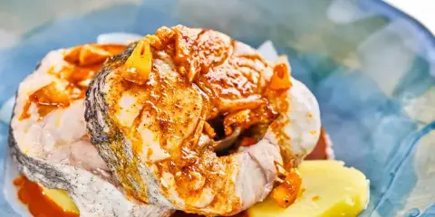 Merluza a la gallega con patatas y salsa de pimentón, servida en un plato azul.
