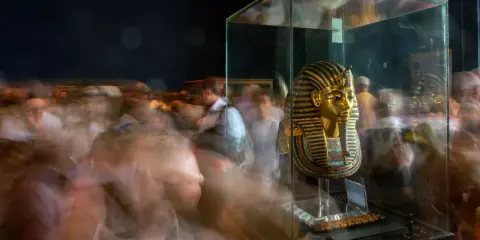 Goldene Maske des Pharao Tutanchamun in einer Vitrine, umgeben von verschwommenen Besuchern.