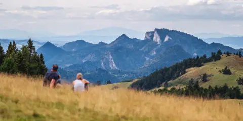 Para odpoczywa na trawiastym wzgórzu, podziwiając malownicze góry. To idealne miejsce, by zobaczyć w Szczawnicy zapierające dech w piersiach widoki.
