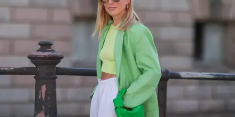 Kobieta w zielonej marynarce i topie typu **krój cropped co to znaczy** – odsłaniający brzuch. W ręku trzyma zieloną torebkę.