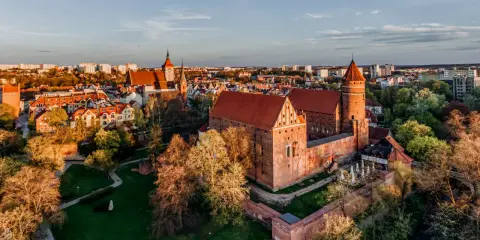 Zachód słońca nad zamkami na Mazurach. Czerwone dachy i ceglane mury w blasku złotej godziny.