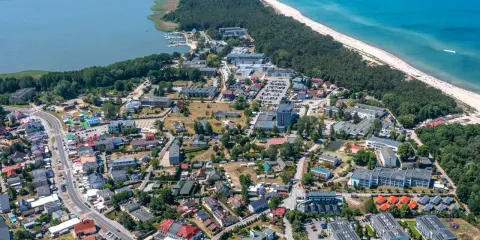 Dąbki atrakcje: widok z lotu ptaka na nadmorską miejscowość z jeziorem, plażą, lasem i zabudowaniami.