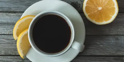 Eine Tasse schwarzer Kaffee mit Zitrone und Zitronenscheiben auf einem Holztisch.