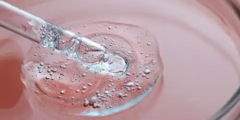 Goutte d'un sérum transparent avec des bulles, sur fond rose. C'est une illustration de ce que sont les peptides, des éléments clés pour la peau.