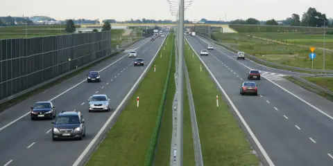 Różne rodzaje dróg: autostrada z pasami ruchu, barierkami i ekranami akustycznymi. Samochody poruszają się po jezdni.