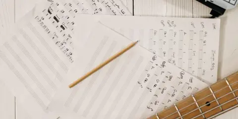 Feuilles de musique manuscrites, un crayon et une guitare. Le matériel parfait pour trouver l'inspiration pour écrire une chanson.