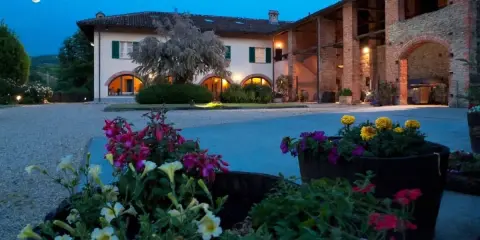 Un casale illuminato al crepuscolo, con fiori colorati in primo piano. Ideale per un weekend degustazione vini Piemonte.